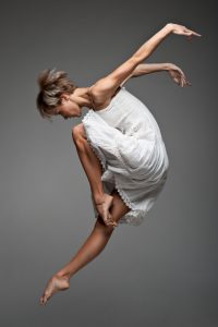 beautiful young caucasian female dancer jumping over gray background